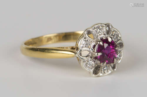 An 18ct gold, ruby and diamond cluster ring, claw set with a circular cut ruby within a pierced