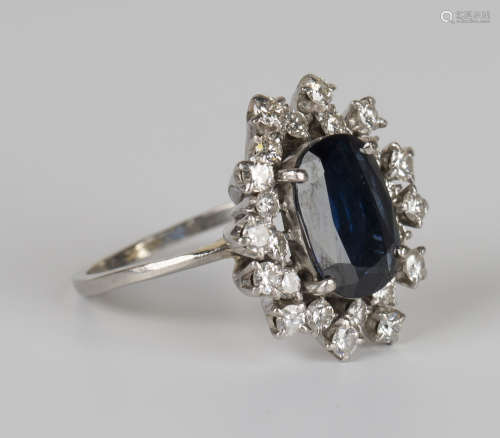 A sapphire and diamond oval cluster ring, claw set with an oval cut sapphire within an abstract