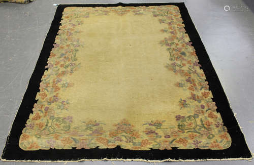 A Chinese rug, mid-20th century, the plain ivory field with a flowering border and plain black outer