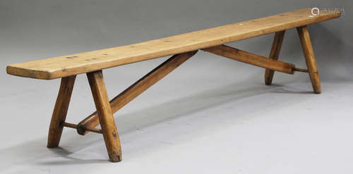 A 19th century primitive fruitwood bench, the long rectangular seat raised on staked legs and