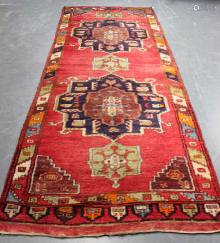 A Turkish runner, 20th century, the red field with two bold blue medallions, within a polychrome