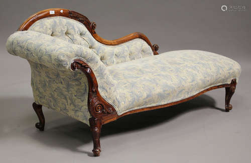 A late Victorian walnut showframe chaise longue, upholstered in a patterned fabric, on carved