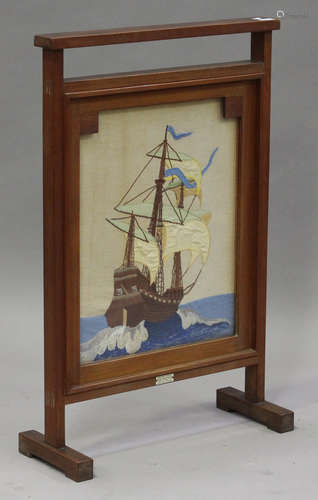 A mid-20th century teak framed firescreen, inset with a needlework panel of a ship and bearing