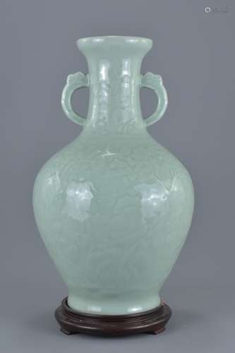 A Chinese celadon porcelain twin handle vase attached to wooden stand. Hole through centre of vase b