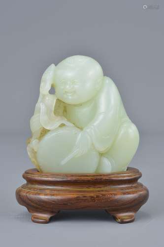 A Chinese 19th century pale celadon jade carving of a boy holding a ruyi sceptre with bat playing a