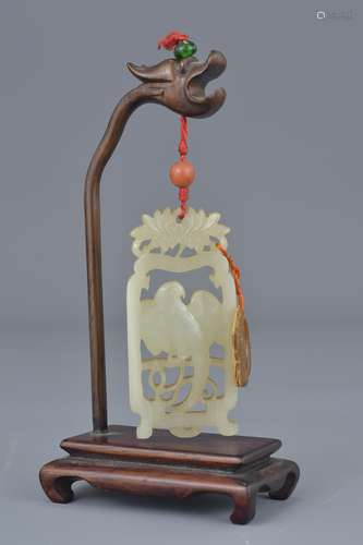 A 19/20th century Chinese carved jade pendant depicting bird in frame suspended from a wooden stand.