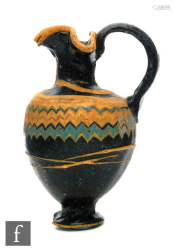 Roman 2nd to 4th Century AD - A miniature dark black glass jug with multi yellow zig zag bands of decoration to the shoulder, on a pedestal foot, height 7.5cm