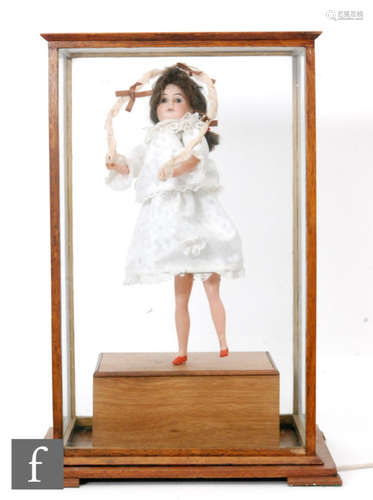 A 20th Century and later constructed German bisque head dancing girl automaton holding a lace edged hoop, plastic limbs in glazed display case, converted to electricity, height 56cm