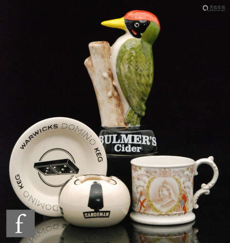 A Carltonware Bulmers Woodpecker advertising figure, height 18.5cm, a Sandeman ashtray, a Wade domino ashtray and an 1899 commemorative mug produced for Harrods stores. (4)