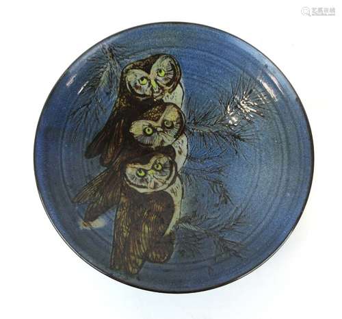 A studio pottery shallow dish decorated with three owls on a branch within a blue ground,