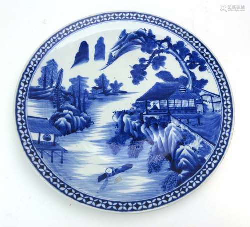 A large Japanese blue and white charger decorated with a village landscape,