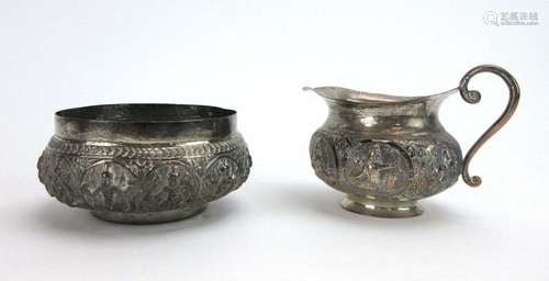 An Anglo-Indian metalware sugar bowl and matching jug, typically relief decorated with deities,