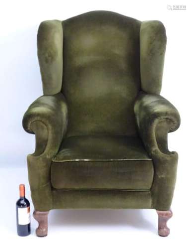 A 20thC green upholstered wingback armchair, raised on