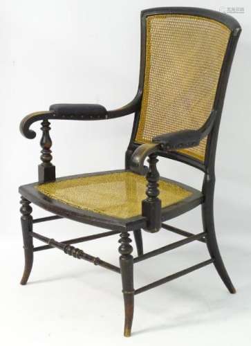 A late 19thC ebonised caned seated open armchair with