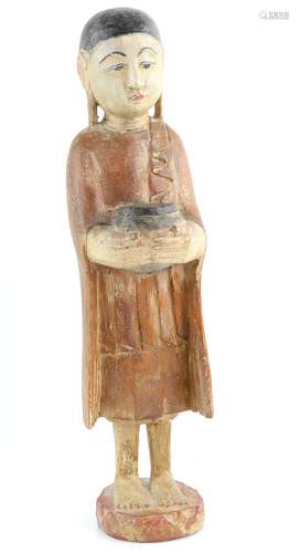 A Burmese, or other South-East Asian, wood figure of a standing, barefooted acolyte, holding an alms