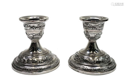 A pair of Indian silver low candlesticks, repousee decorated with village scenes,