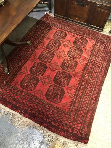 A vintage red ground Afghan rug, the mid-red ground with two rows of guls