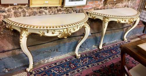 A companion pair of Italianate ivory and gilt painted demi-lune console tables