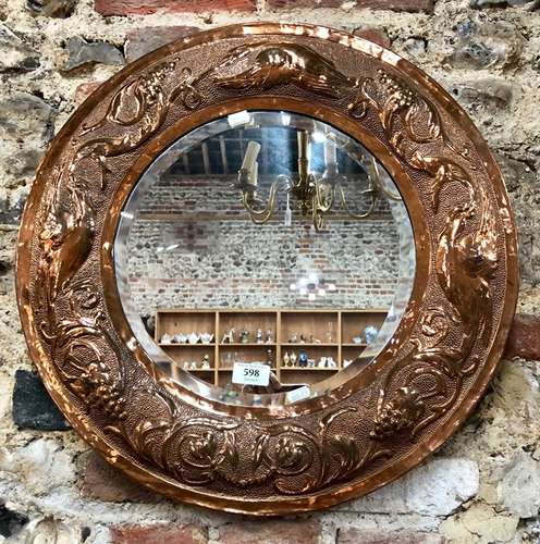 An Arts & Crafts circular hammered and relief decorated copper wall mirror