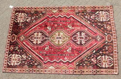A PERSIAN TRIBAL SHIRAZ QASHQAI CARPET with a large motif on a red ground. 11ft 6ins x 5ft 6ins.