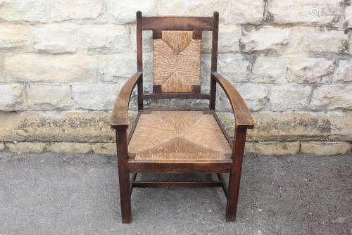 An Oak Arts & Crafts Armchair, having a rush back rest and seat