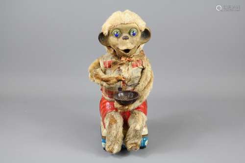 A Vintage Monkey Automaton; the seated monkey is holding a spoon and porridge bowl, he has a red shorts and check shirt and bright blue eyes, approx 28 cms h