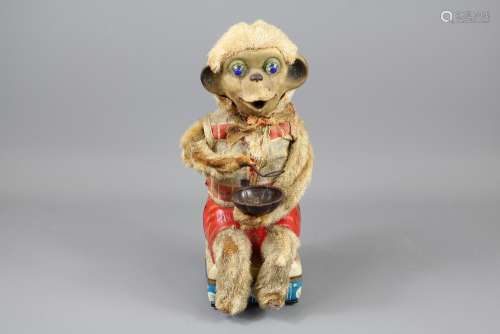 A Vintage Monkey Automaton; the seated monkey is holding a spoon and porridge bowl, he has a red shorts and check shirt and bright blue eyes, approx 28 cms h