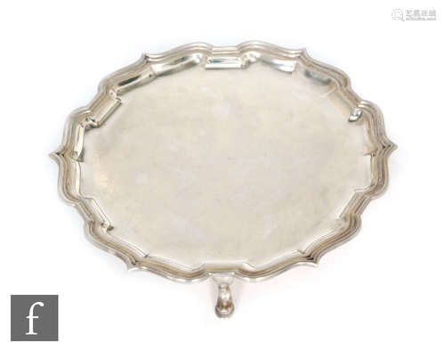 A hallmarked silver circular salver of plain form with pie crust edge and raised on three pad