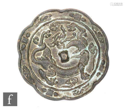 A Chinese bronze mirror, of circular scalloped form, cast in relief to the front with a dragon and