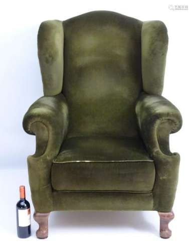 A 20thC green upholstered wingback armchair, raised on